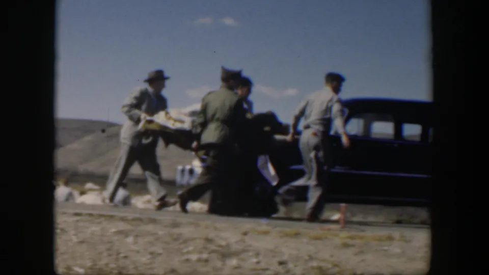 A group in mid-century clothing carries a person toward a dark sedan in the Texas landscape shown in the clip metadata.