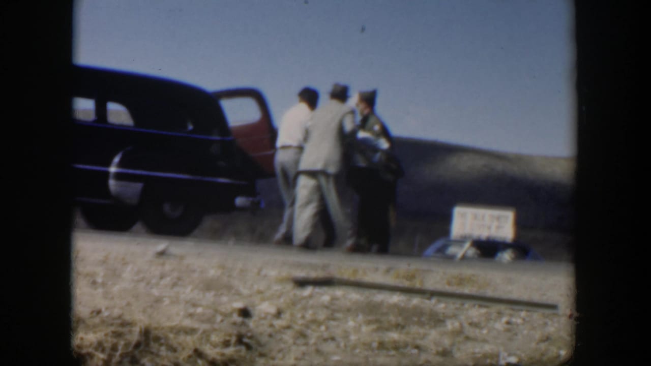 Men stand near an open sedan door while handling a covered stretcher.