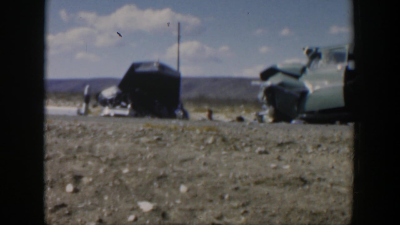 Two damaged cars on a rural roadside with debris scattered near the shoulder.