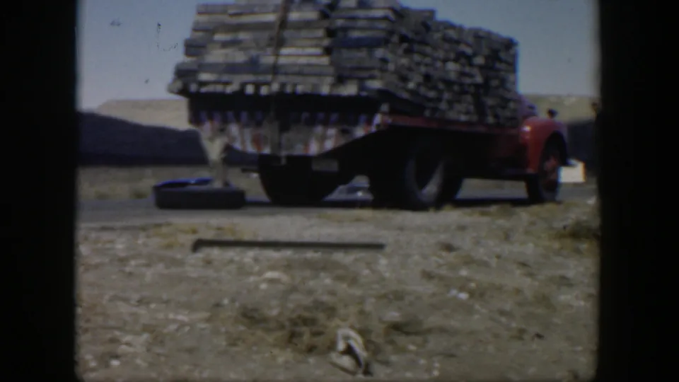 1951 Texas 8mm frame showing a red flatbed truck loaded with stacked material near roadside debris after the crash.