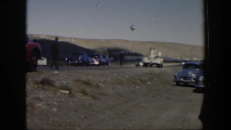 1951 Texas roadside view with dark sedans, a light utility-style truck, and a person walking across the dusty open road.