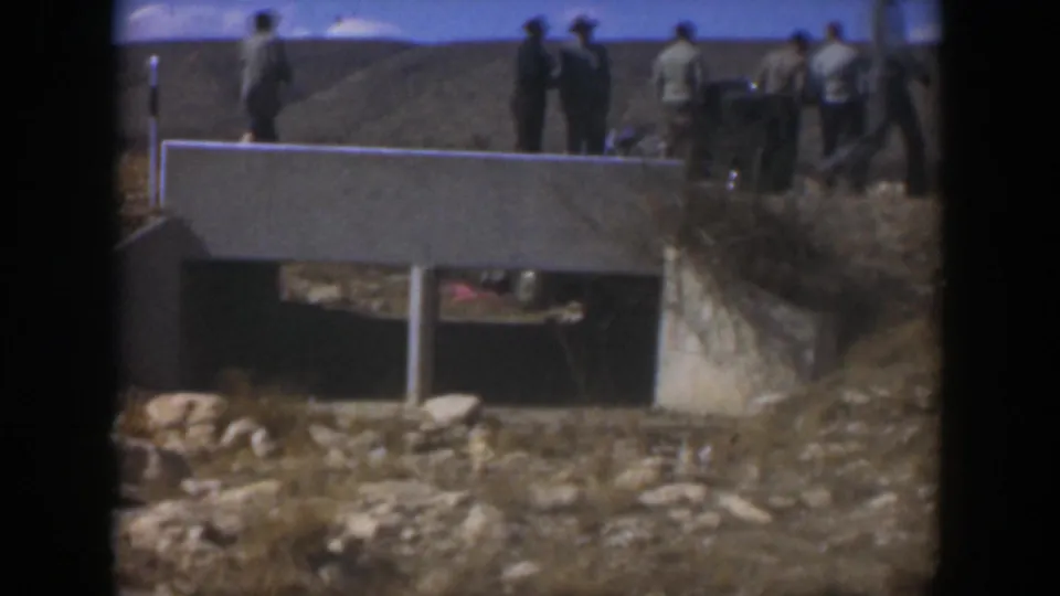 1951 Texas 8mm frame showing men, several wearing hats, gathered near a concrete bridge in a dry open landscape.