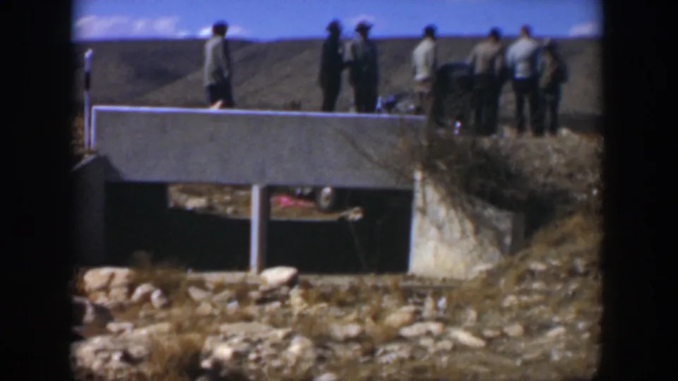 1951 Texas frame showing a small group of men near a concrete bridge, with cars partly visible in the open landscape.