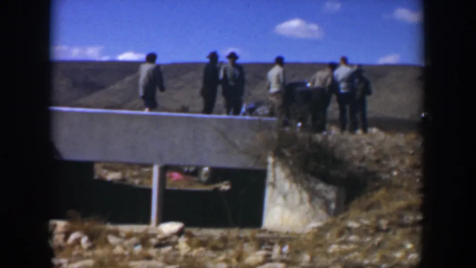 1951 Texas 8mm frame showing men gathered near a crumpled green car by a concrete culvert in a dry field.