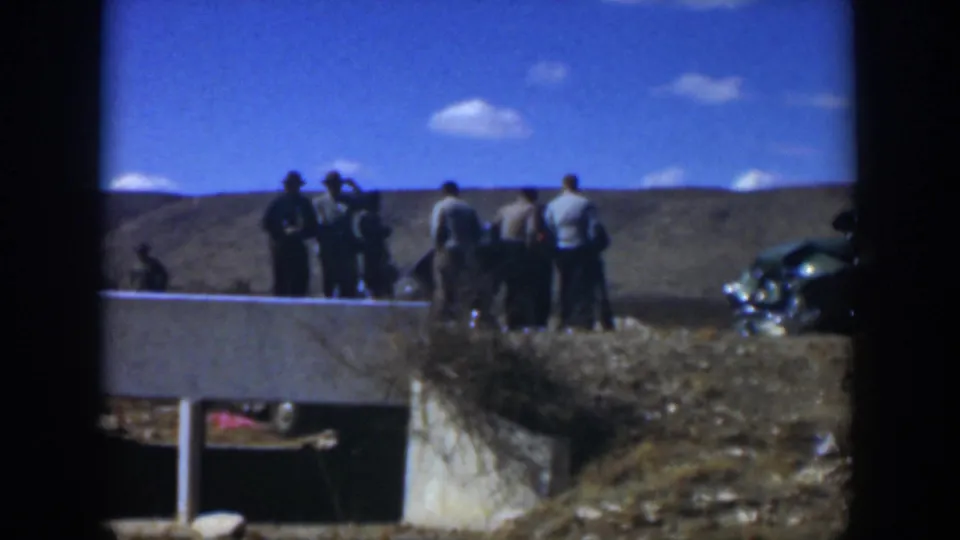 1951 Texas home-movie frame of men beside a concrete culvert, with a damaged green car partly visible at right.