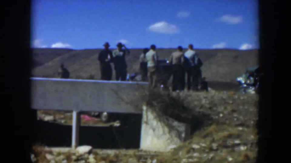 1951 Texas home-movie frame showing people gathered outdoors near a low wall, with dry ground and open sky behind them.