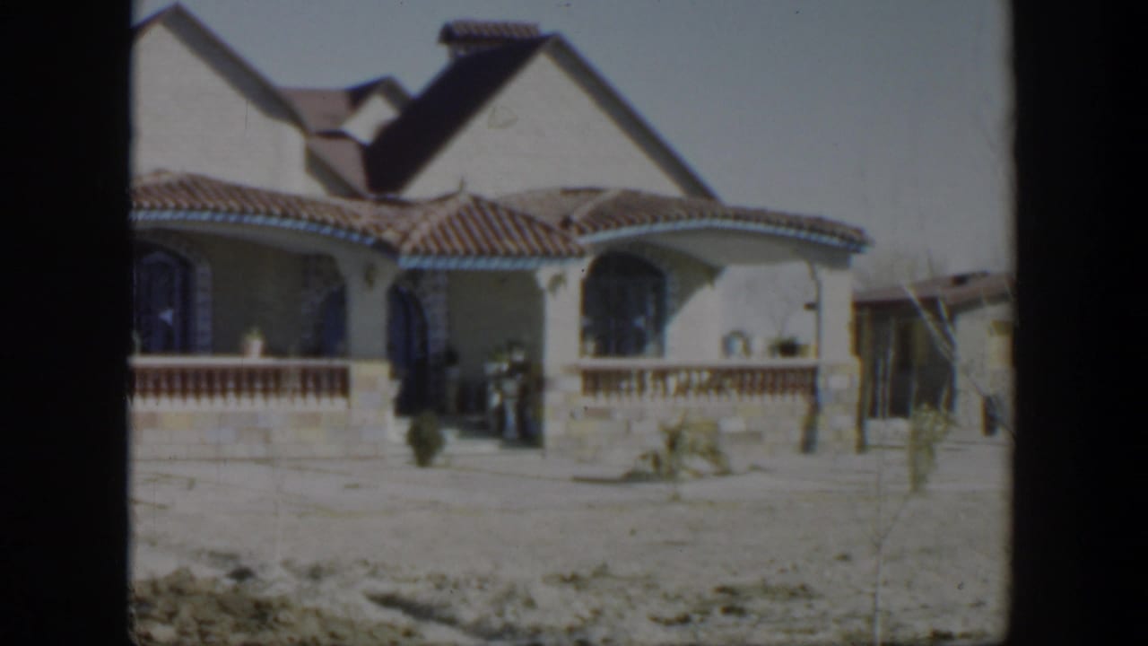 Stucco house with tiled roof, arched windows, porch railing, and a person by the entry.