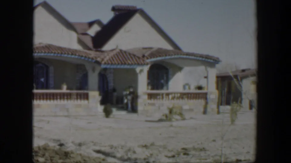 1951 Texas exterior view of a stucco residential house with tiled roof, arched openings, porch railing, and a person near the entrance.