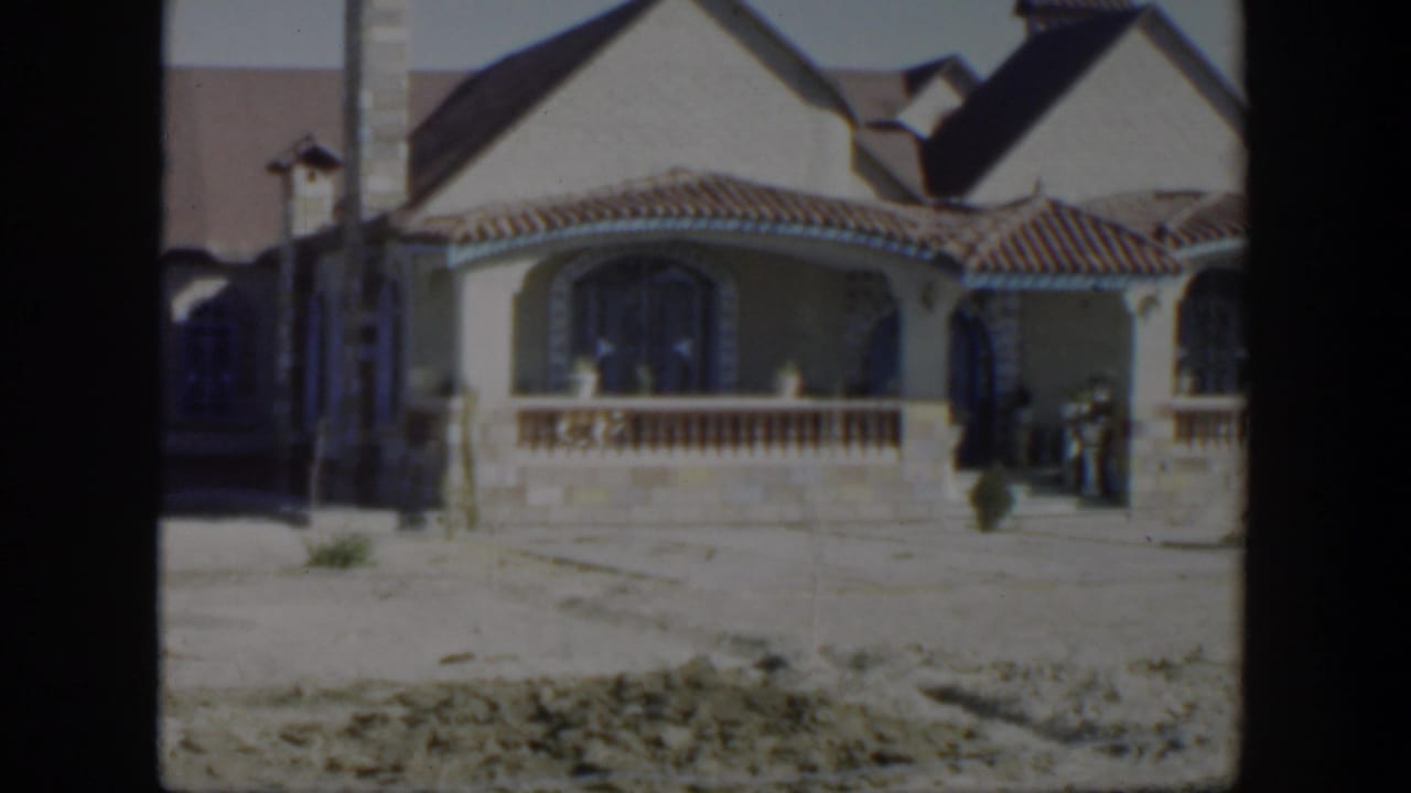 Large stucco house with tiled roof and arched porch in a bare yard.
