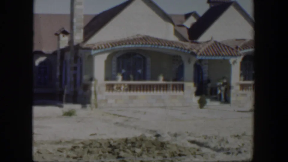 1951 Texas 8mm frame showing a large stucco house with a tiled roof, arched porch, chimney, and open treeless yard.