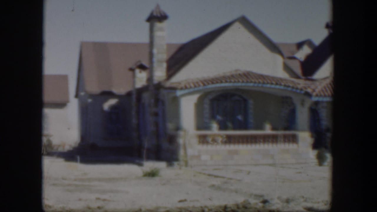 Stucco house and porch with distant figures near the entrance.