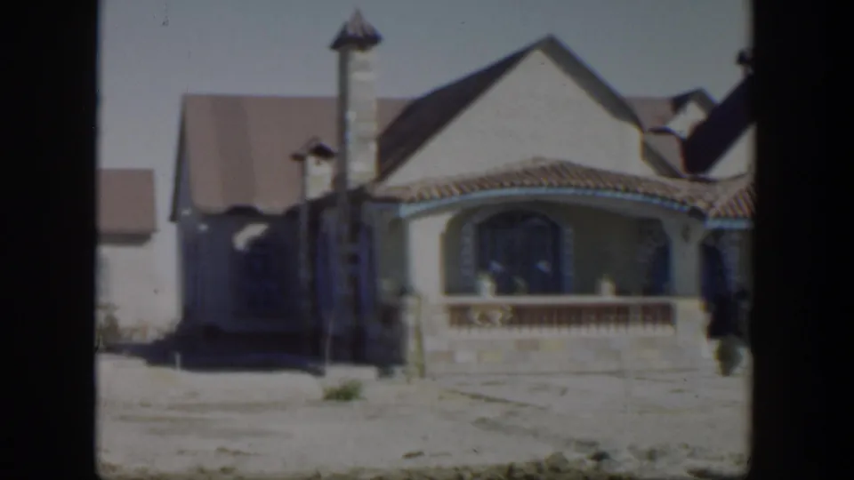 1951 Texas home-movie frame showing the main stucco house, arched porch, tiled roof, and small distant figures by the doorway.