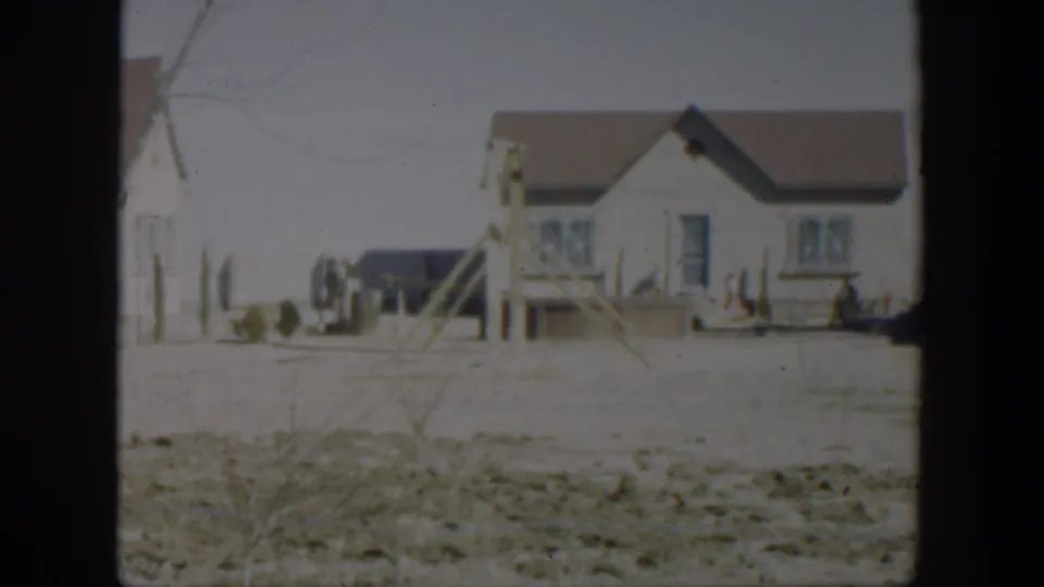 1951 Texas residential exterior with a small white house, porch steps, fence posts, dry ground, and a dark parked vehicle nearby.
