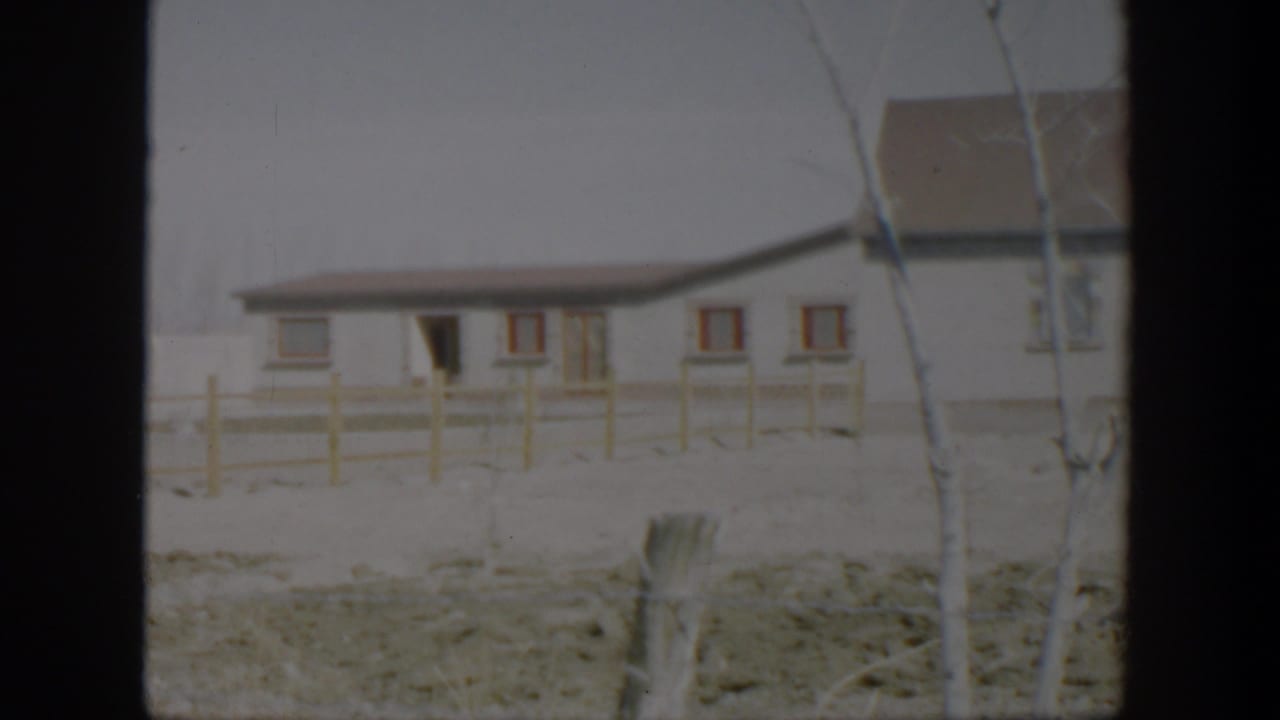 White house with red-trimmed windows, wooden fence, bare trees, and snow on the ground.