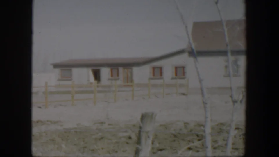 1951 Texas residential exterior with a white house, red-trimmed windows, bare tree limbs, fence posts, and snowy ground.