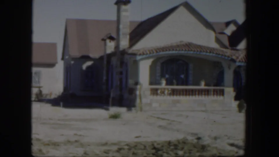 1951 Texas home-movie frame showing a larger residential house with arched porch details, tiled roof, driveway, and muted winter yard.