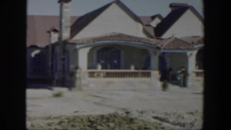 1951 Texas residential exterior with an arched porch, tiled roof, driveway, and indistinct dark shapes near the right side.