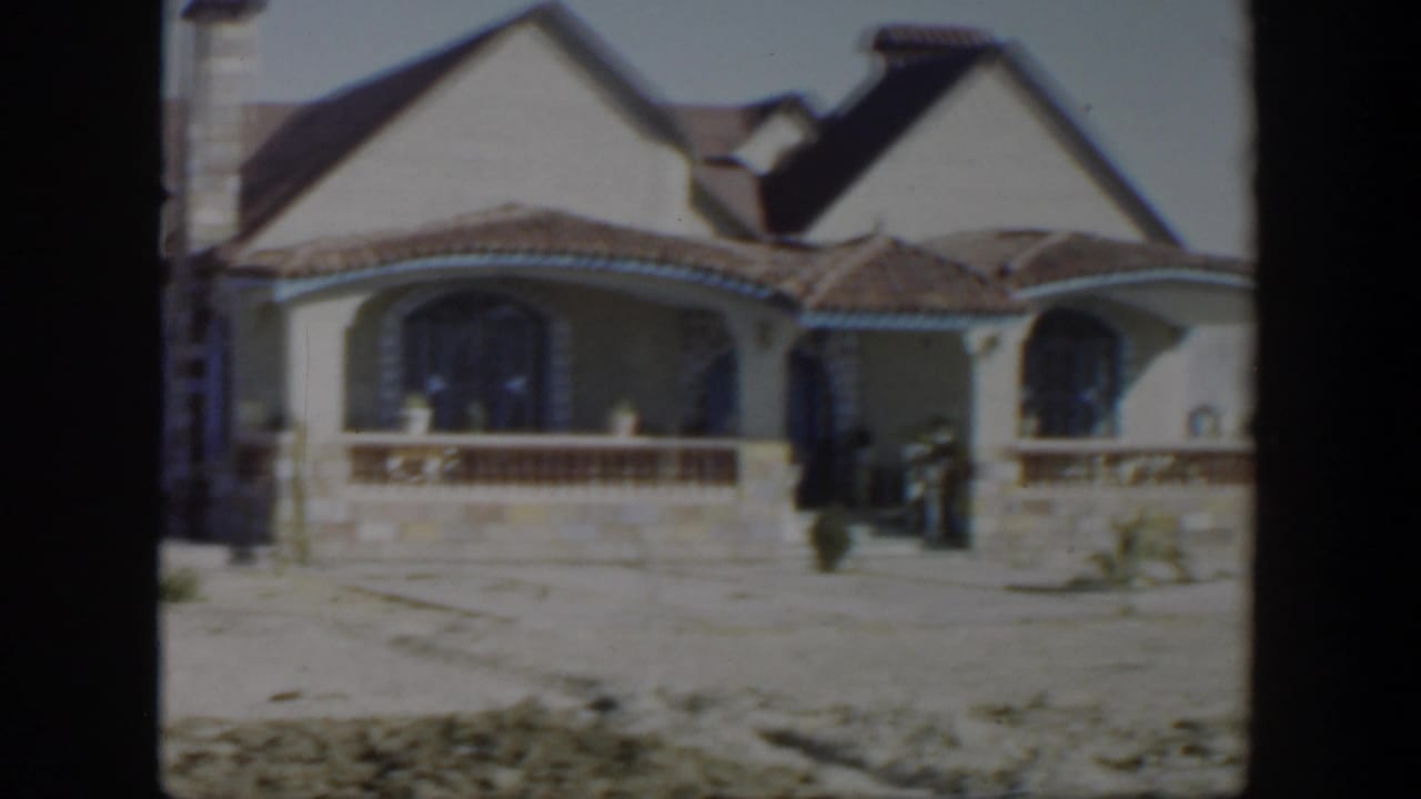 Spanish-style house with tiled roof, arched windows, porch railing, and dry front yard.