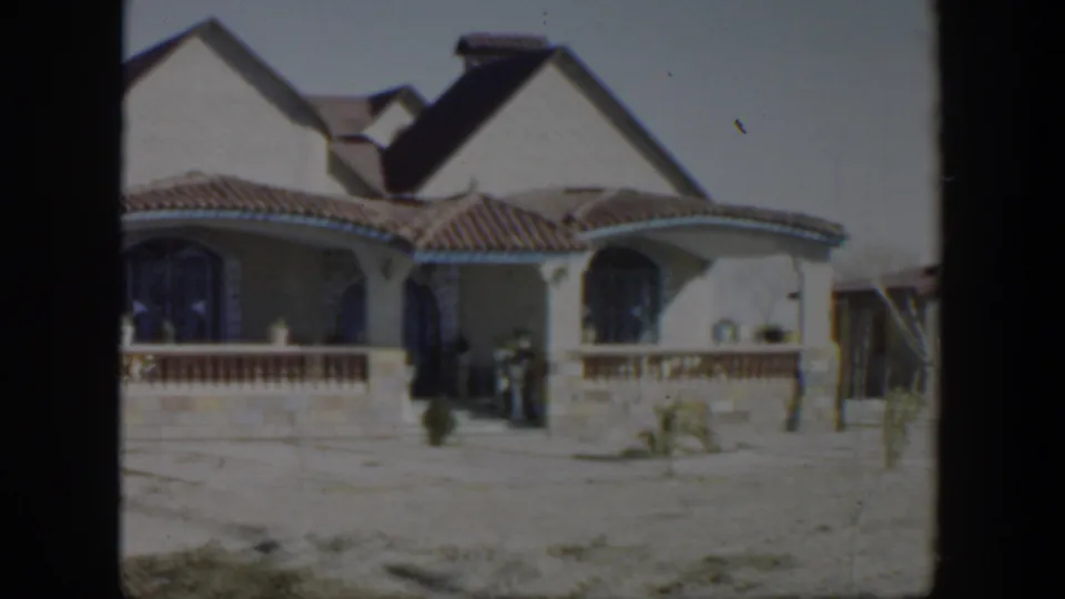 Texas 1951 8mm frame showing the house facade from a slightly shifted angle, including arched windows, tiled roof, and entry area.