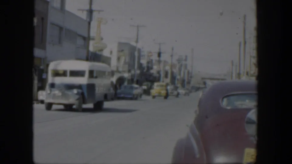 A 1951 Texas city street view captures a white bus passing cars and storefronts, with a rounded vehicle body at the right edge.