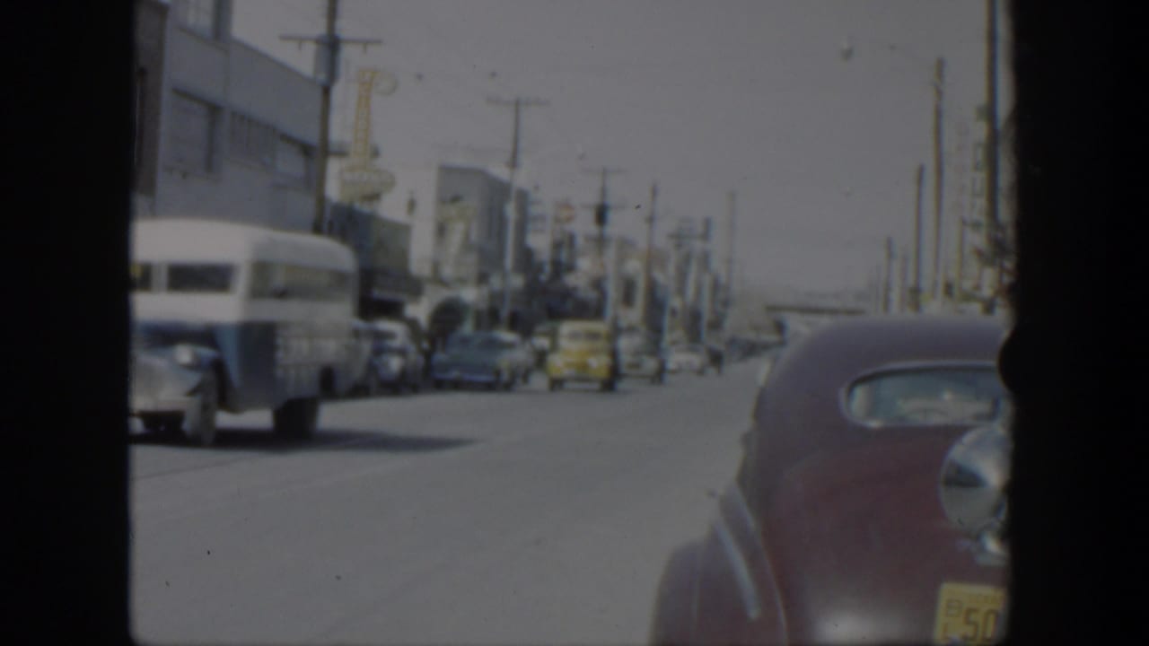 Busy sunlit street with vintage cars, a white bus, and a maroon sedan near the camera.