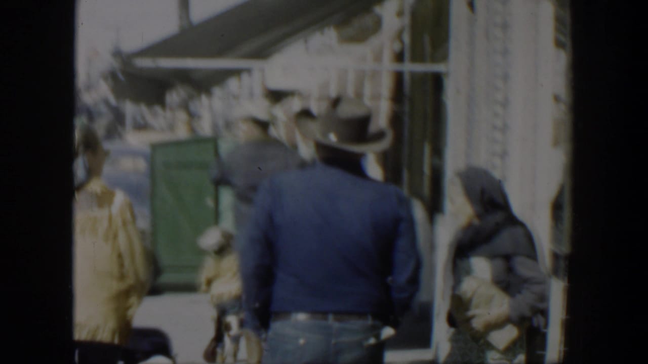 1951 Texas 8mm frame showing pedestrians on a commercial sidewalk, including a man in a cowboy hat near storefront awnings.