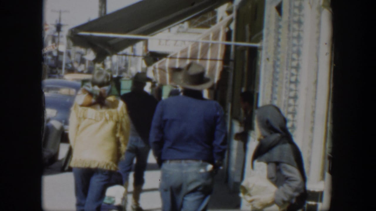 1951 Texas street view with pedestrians walking past awnings and storefronts, with mid-century cars visible along the road.