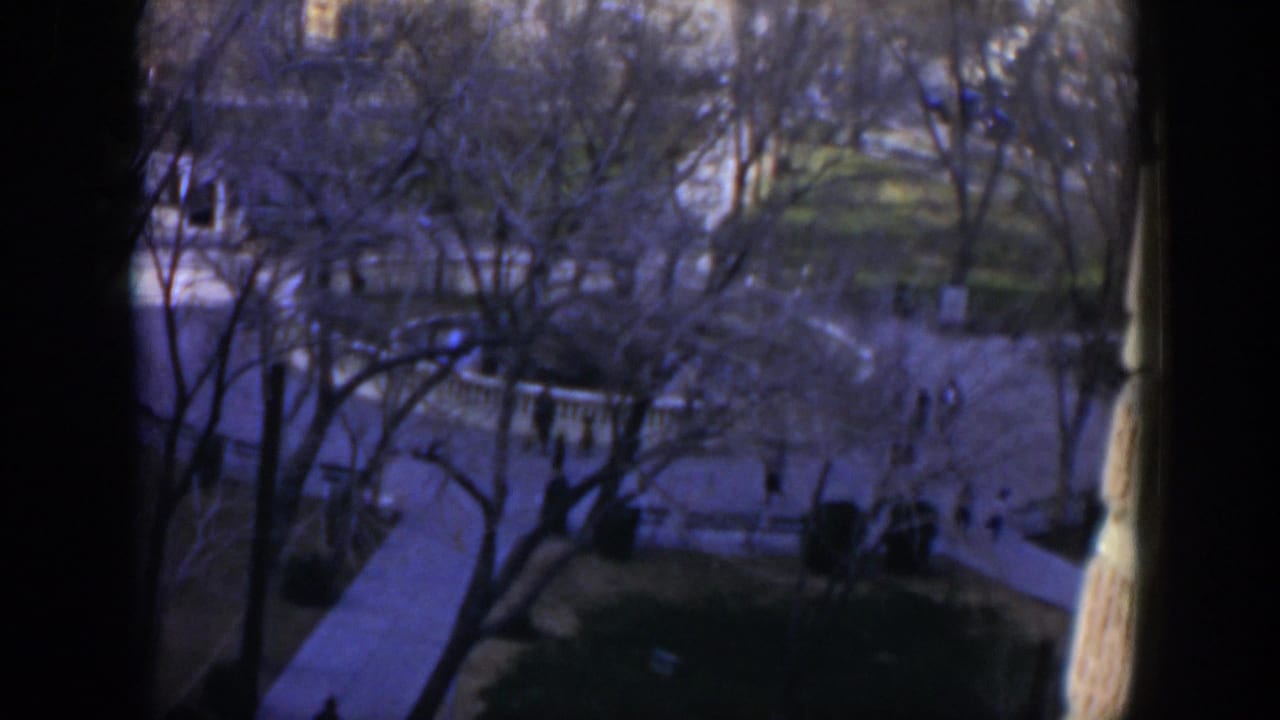 High-angle 1951 Texas home-movie view of a shaded courtyard where distant people walk between white railings and trees.