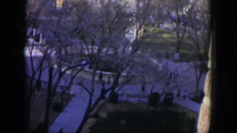 High-angle 1951 Texas home-movie view of a shaded courtyard where distant people walk between white railings and trees.