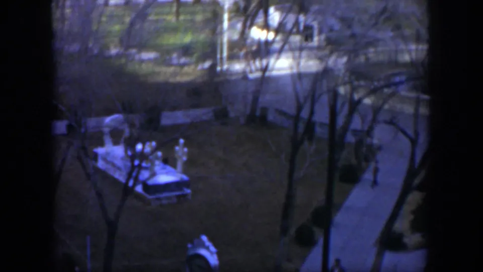 1951 Texas home-movie frame of a park from above, with bare trees, a sidewalk, dark window edges, and a distant person near the path.