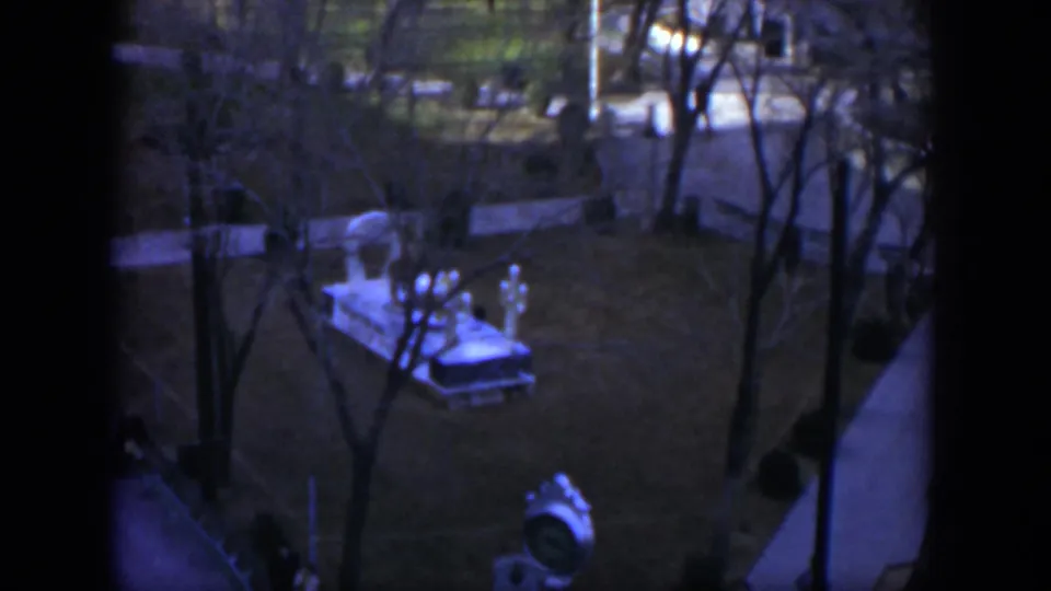 Blue-purple 8mm frame from 1951 Texas showing a distant park through window framing, with bare trees, walkways, lamps, and a white structure.