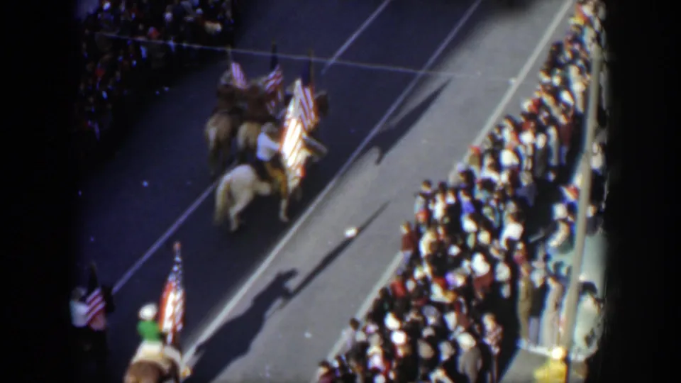 Late in the clip, a rider carrying a United States flag follows other mounted parade participants along the Texas street route.