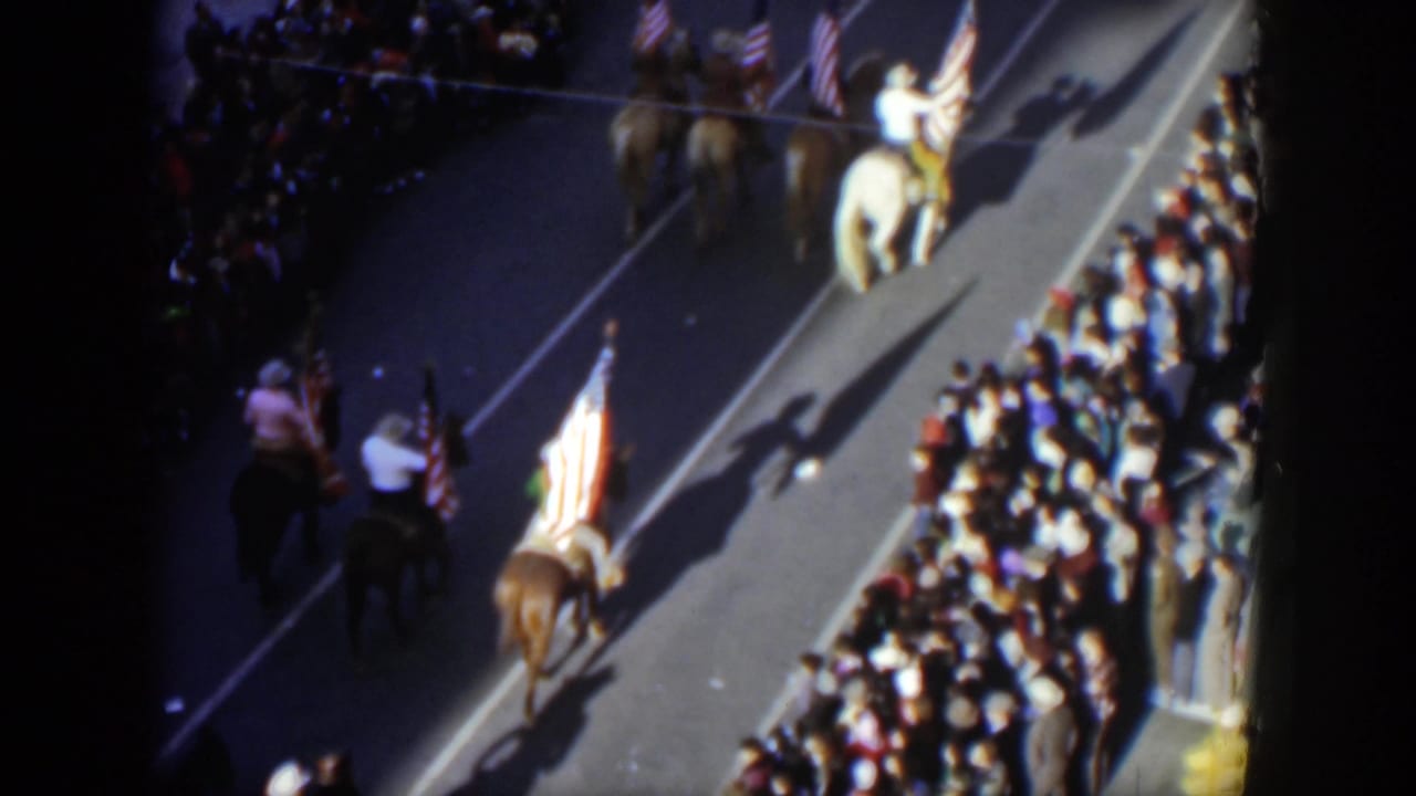 Elevated 1951 Texas parade view with horseback riders carrying American flags beside a tightly packed curbside crowd.
