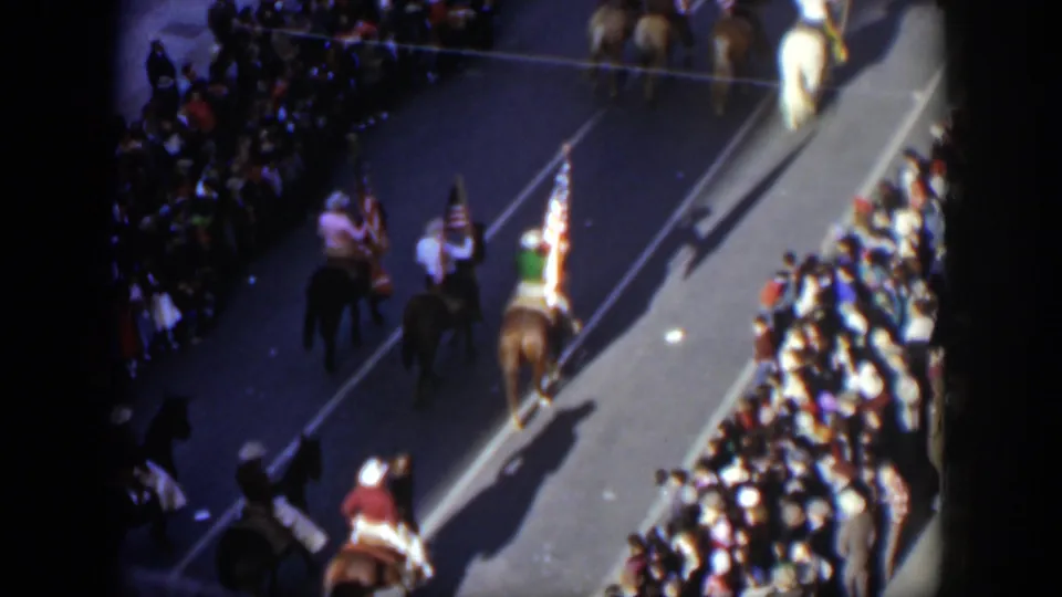 1951 Texas home-movie frame showing multiple horseback riders with flags passing a crowded parade route from above.