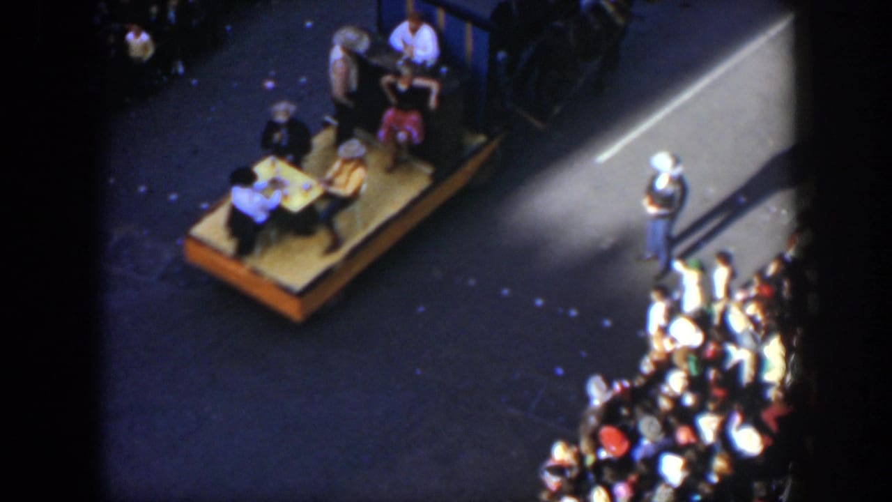 1951 Texas 8mm frame showing a horse-drawn parade platform with seated performers and spectators along the street.