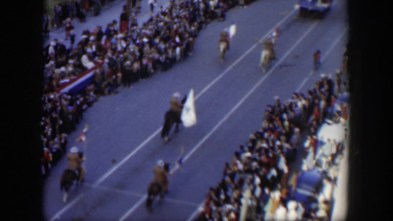 Flag-bearing riders continue down the street between large crowds on both sides.
