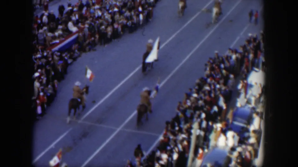 1951 Texas parade frame showing riders on horseback with flags, including a small tricolor flag, moving through a crowded street scene.