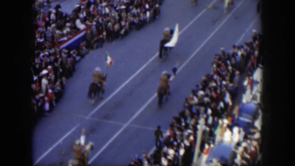 Elevated 1951 Texas home-movie view of mounted flag bearers riding through a city parade with crowds and blue seating visible at the curb.