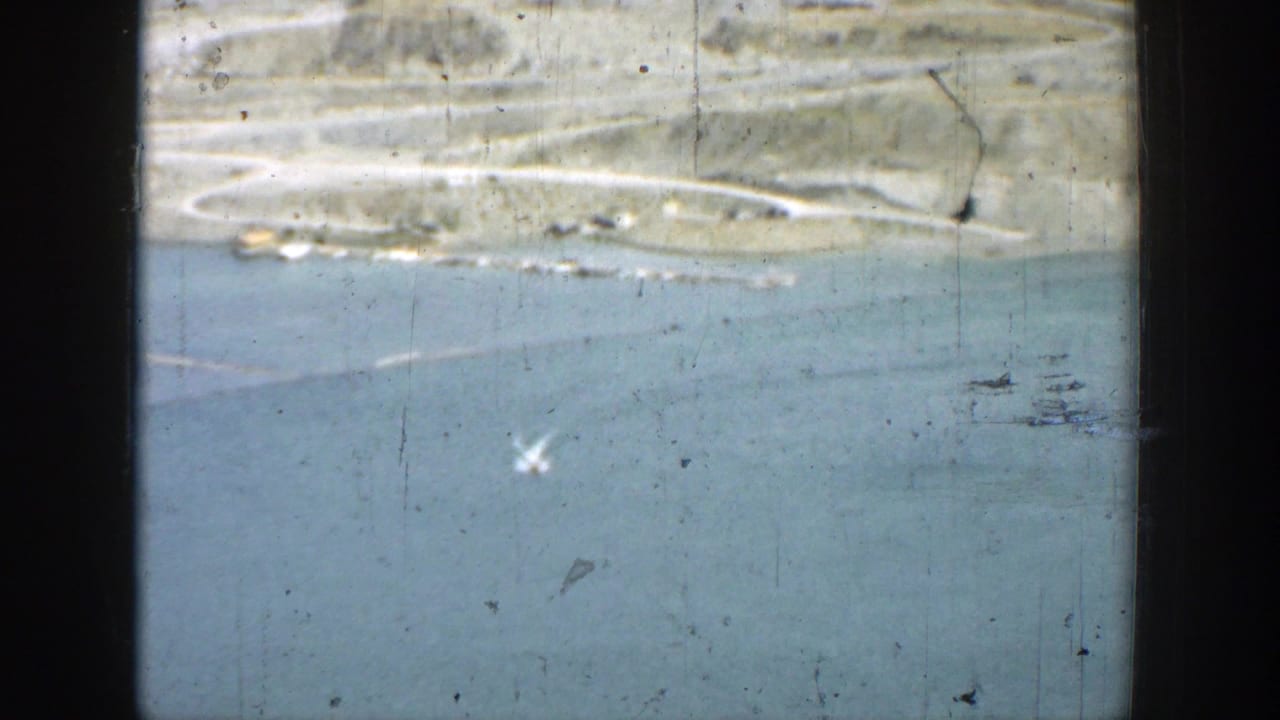 1937 California 8mm view of blue reservoir water, dry hills, and a distant road or shoreline seen through worn film texture.