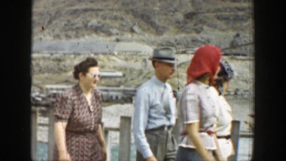 1937 California home-movie frame showing adults in period attire near a wooden fence with dry hills beyond.
