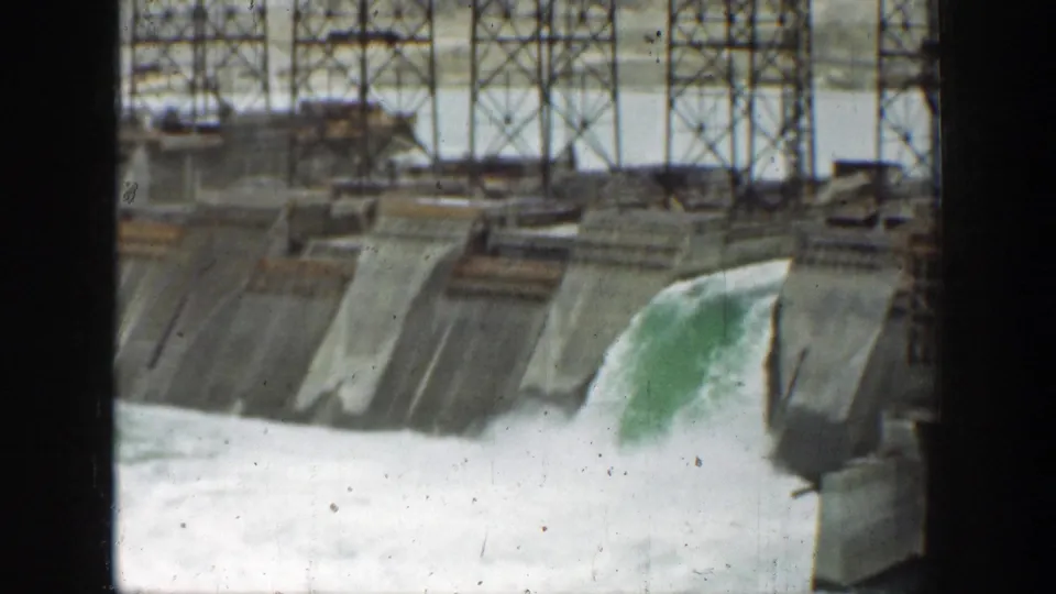 1937 California dam view with water pouring through a concrete spillway and metal framework visible above the structure.
