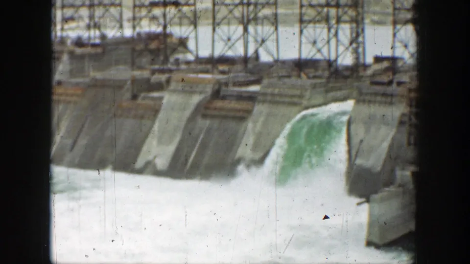 Handheld 8mm view of a California dam spillway with white water moving below sloped concrete faces and metal supports.