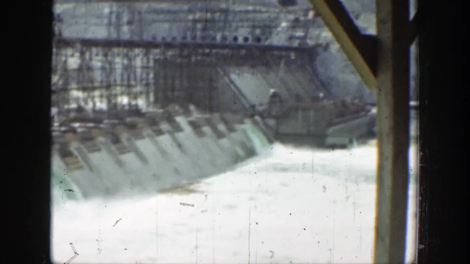 1937 California frame showing a dam or water-control structure with turbulent runoff, concrete spillway panels, and visible film gate edges.