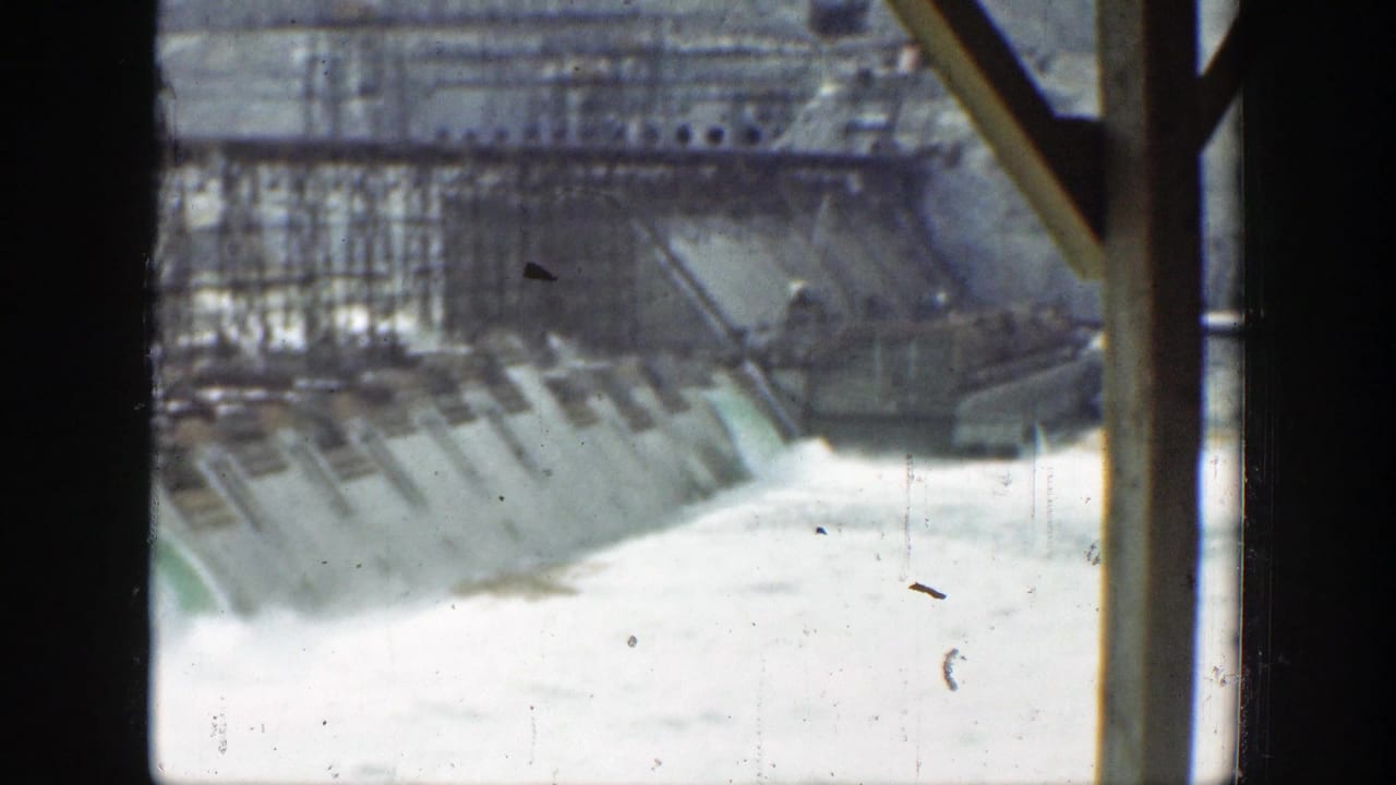Dam spillway and cascading water seen through dark vertical window framing.