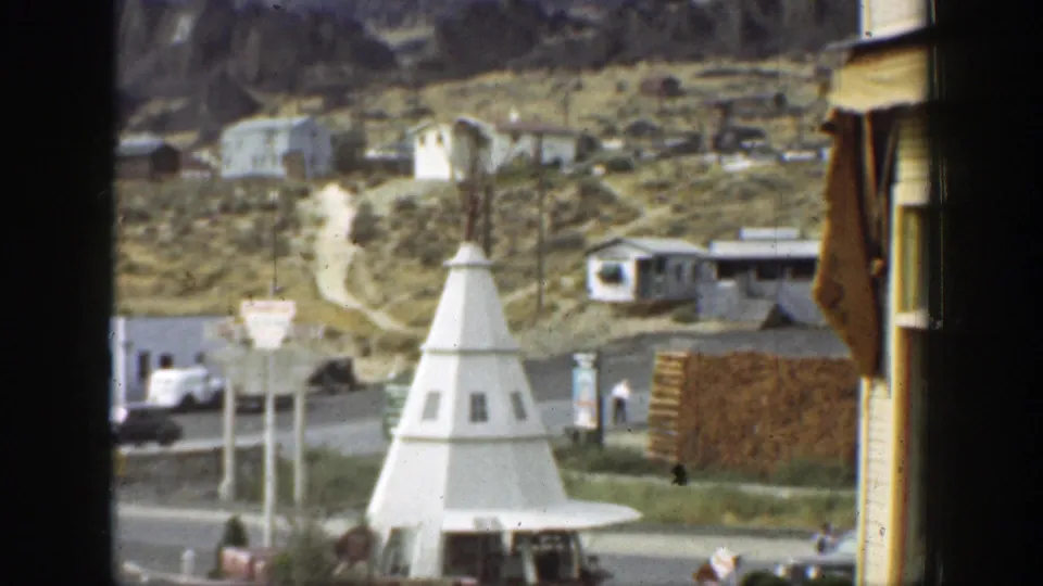 1937 California home-movie frame showing a hillside town street, dirt road, cars, buildings, and a white cone-shaped structure.