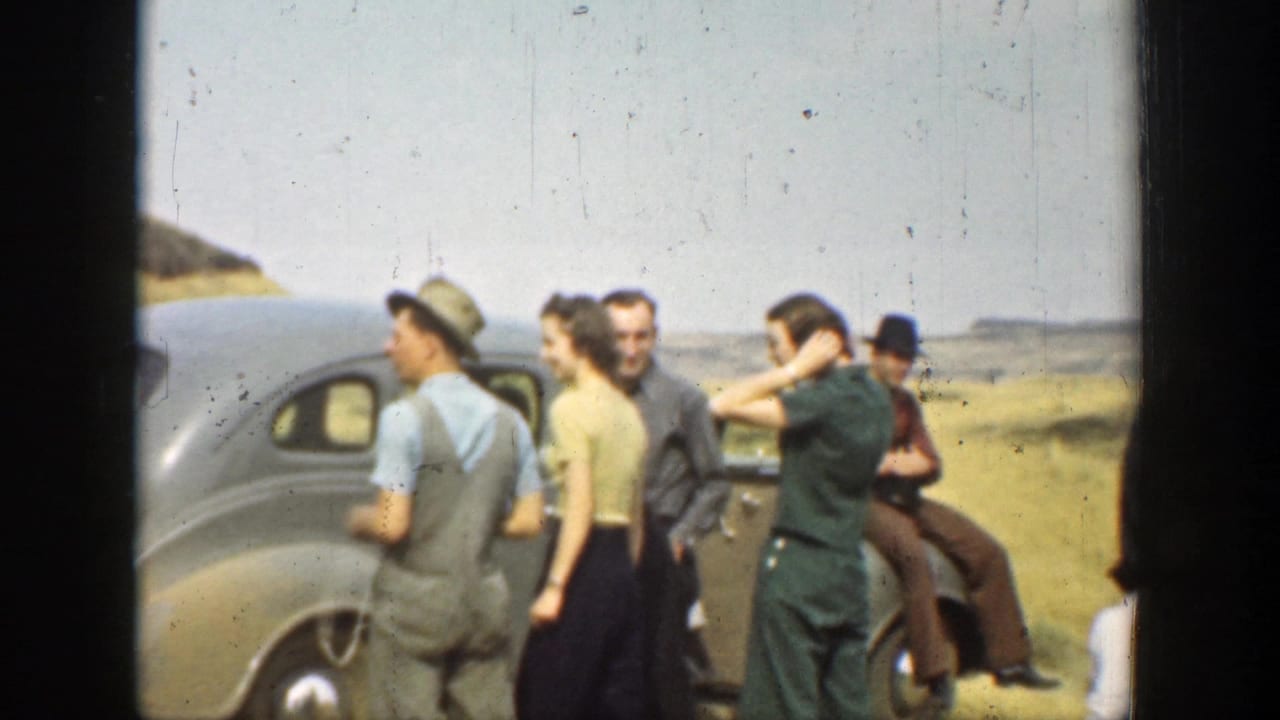 1937 California home-movie frame showing men and women gathered beside parked cars in an open hillside landscape.