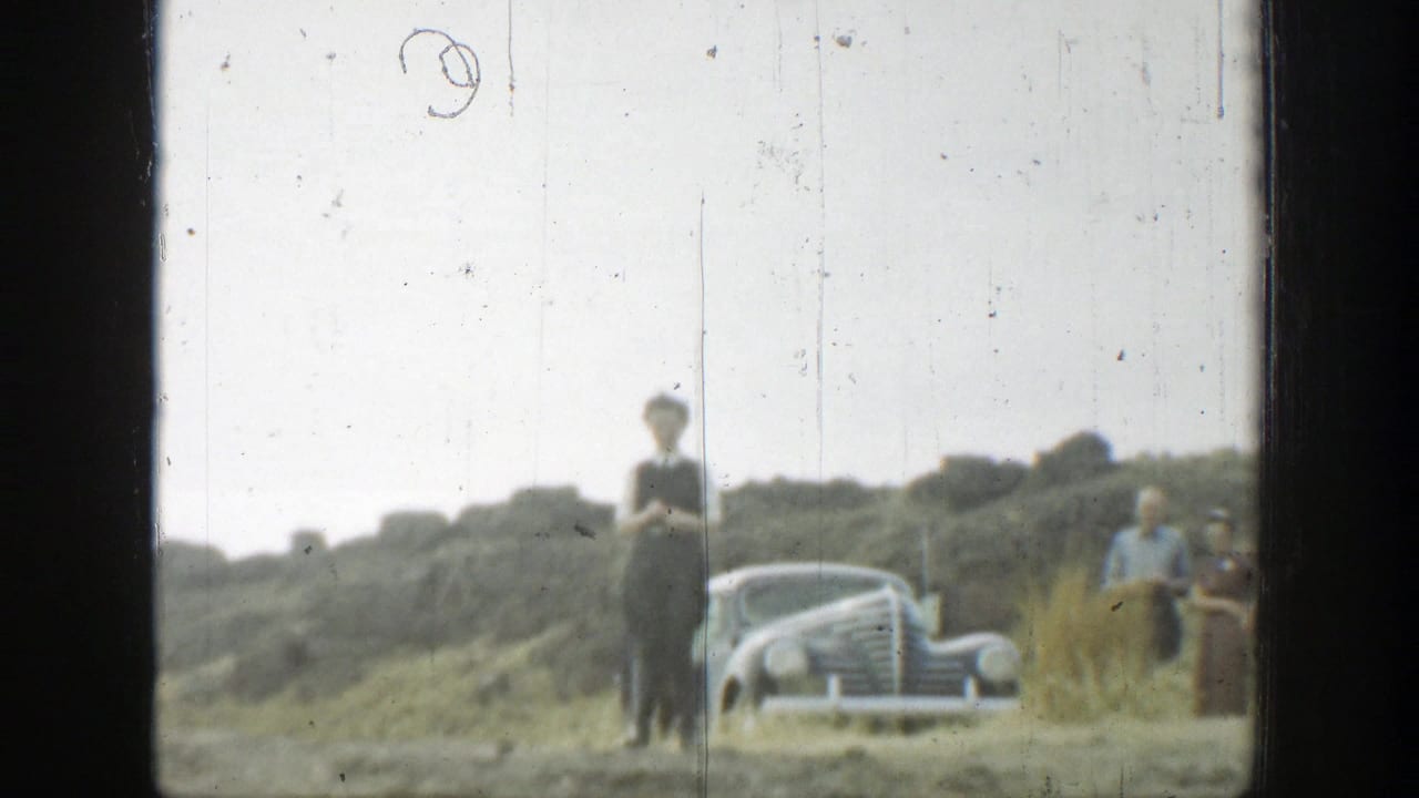 People stand near a vintage car beside a dry hillside trail.