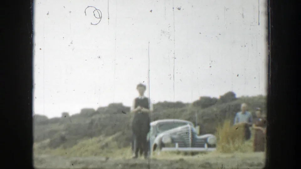1937 California 8mm frame showing people near a rounded vintage car on dry hillside terrain.