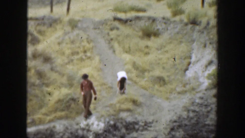 Two hikers walk on a rugged dirt path through dry California hillside terrain in a 1937 home-movie frame.