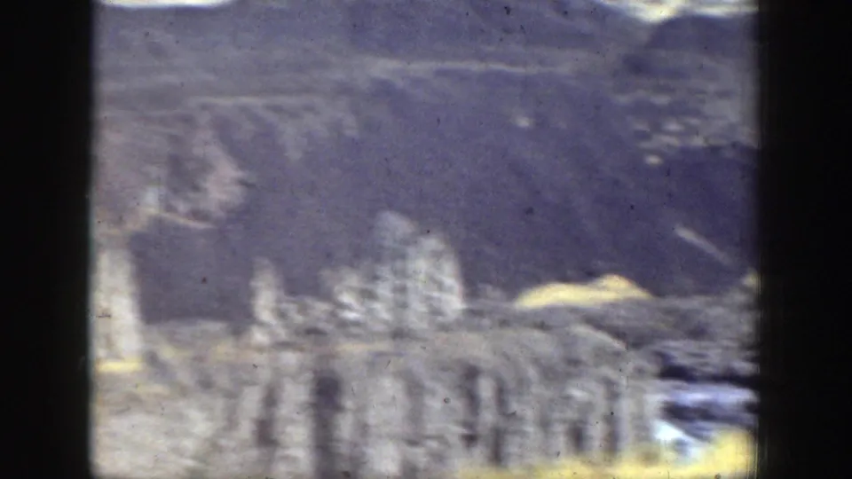 Soft, blurred 8mm view of a rocky hillside or cliff face with light brush and uneven terrain.